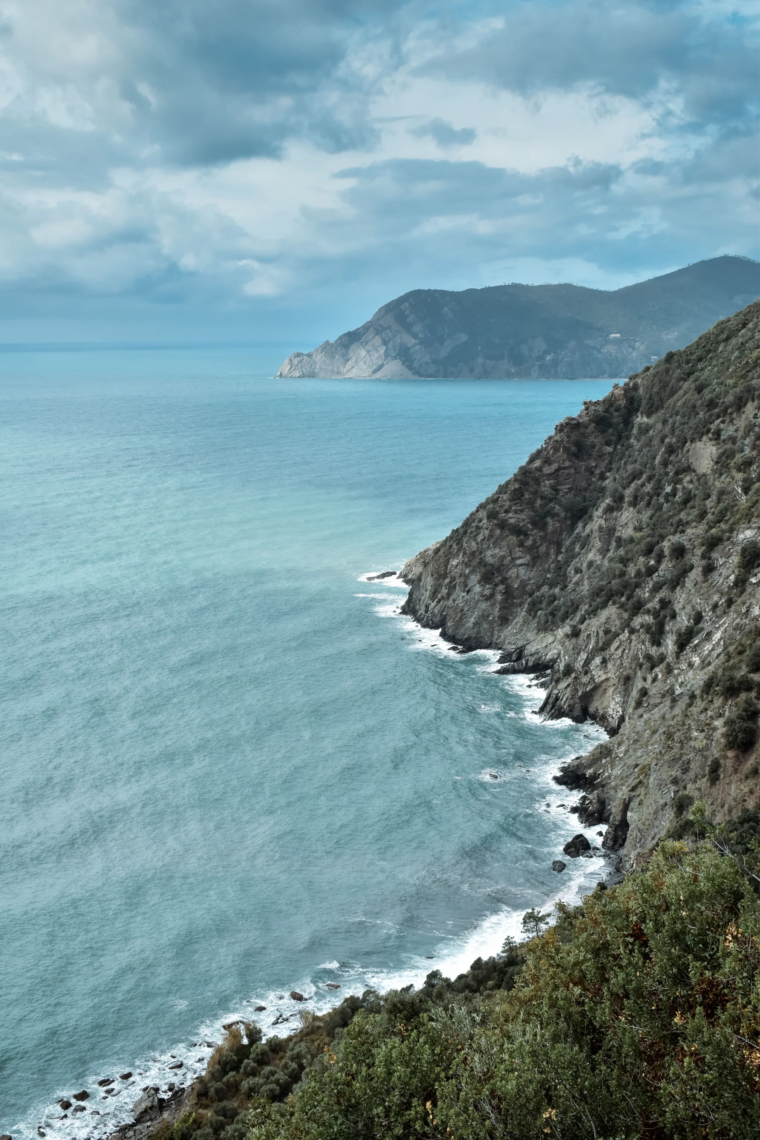 Explore the breathtaking Ligurian coastline with dramatic cliffs and azure waters under a cloudy sky